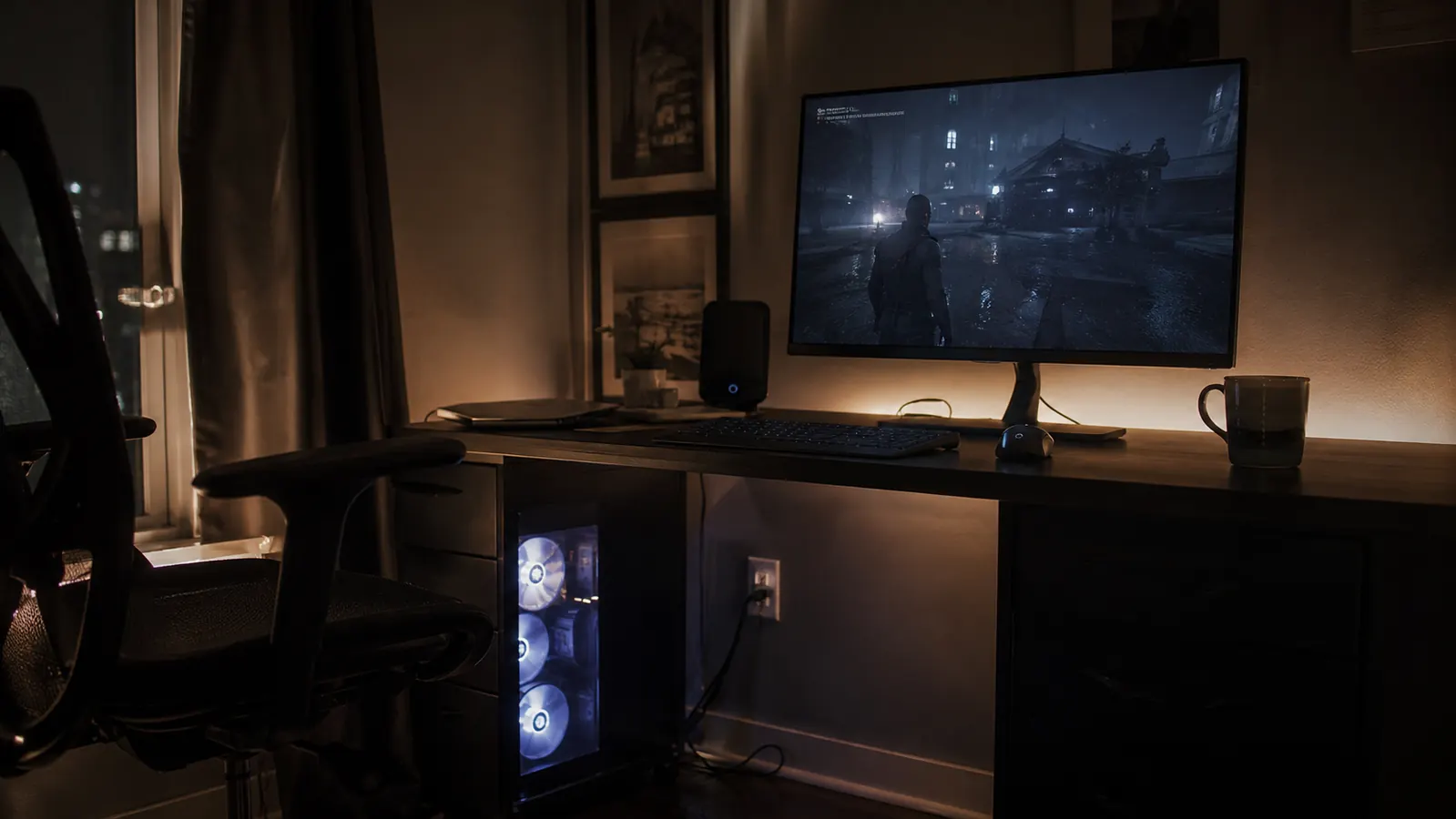 Gaming PC tower on the floor under a desk at night, monitor glowing in a dark home office
