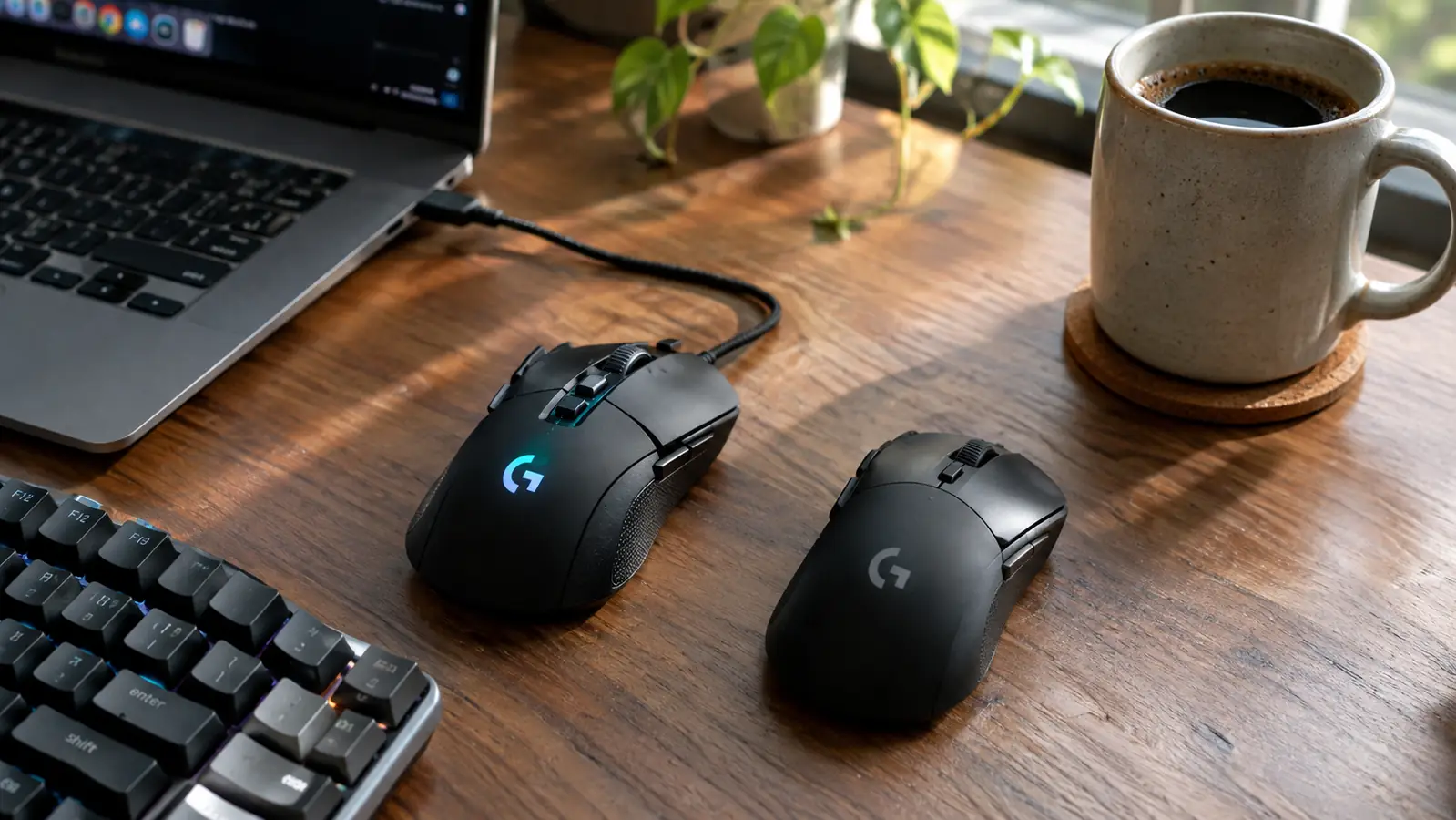 Two gaming mice side by side on a wooden desk, one connected by a braided cable and the other without a cable, with a keyboard and coffee mug nearby